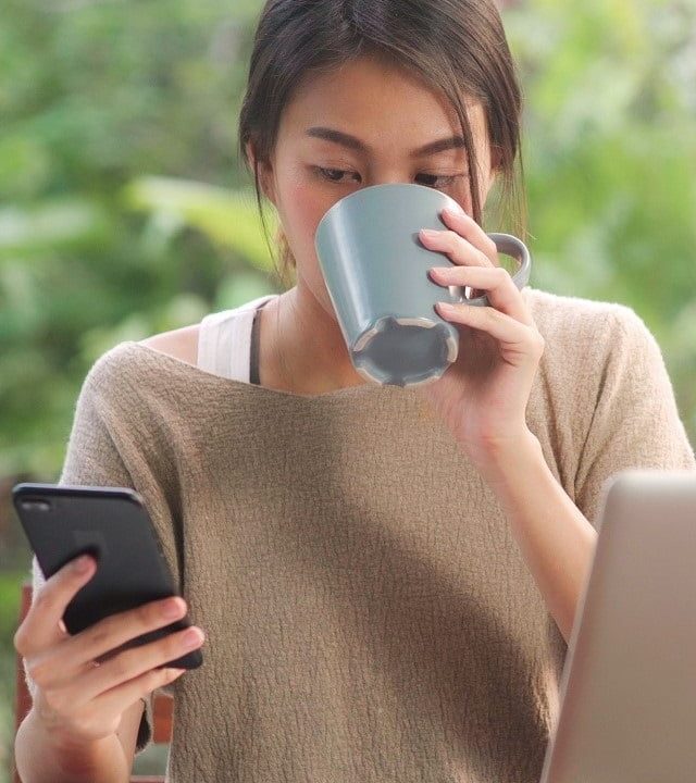 Freelance Asian woman working at home, business female working o Freelance Asian woman working at home, business female working on laptop and using mobile phone drinking coffee sitting on table in the garden in morning. Lifestyle women working at home concept.
